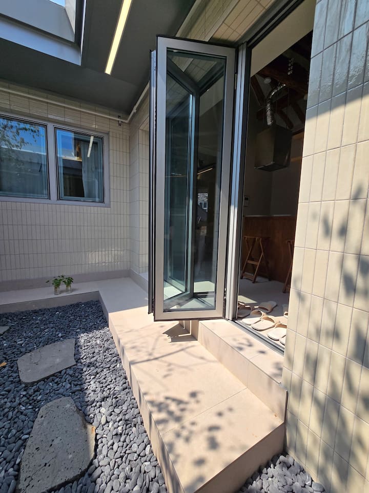 폴딩도어를 열고 들어가면 작고 세련된 주방이 나타납니다. 깨끗한 유리창을 통해 정원을 감상할 수 있습니다. 전통 한옥의 댓돌 문화를  느낄 수 있는 곳에서 신발을 벗고  실내화를 신고 입장하면 됩니다. 